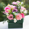 A bouquet of pink and purple roses and filler flowers displayed in a dark green wooden box.