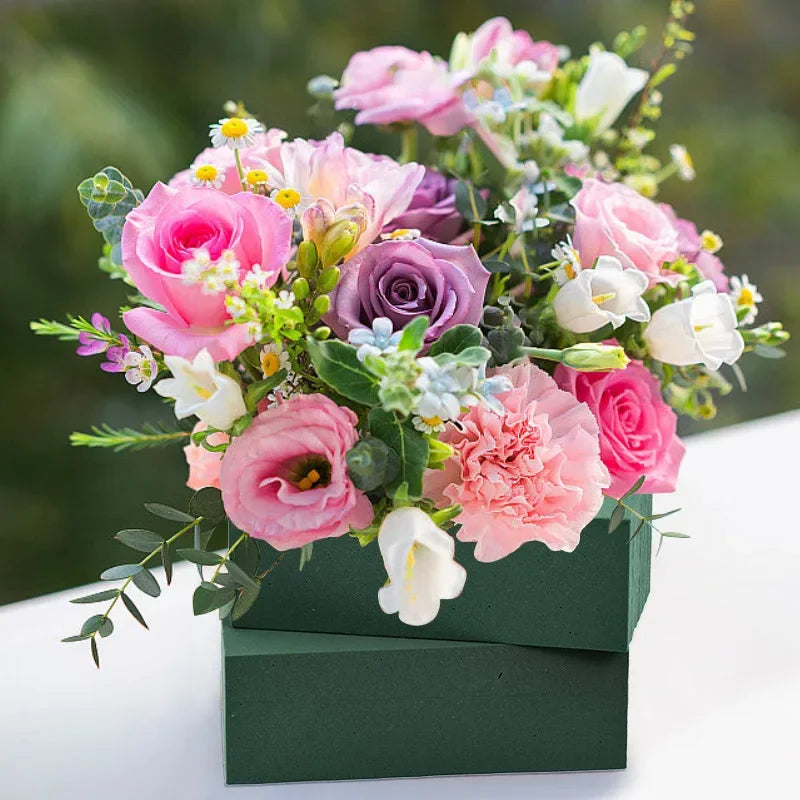 A bouquet of pink and purple roses and filler flowers displayed in a dark green wooden box.