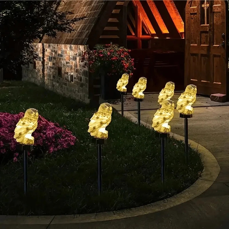 A row of solar-powered owl garden stake lights illuminates golden owls in a garden setting.