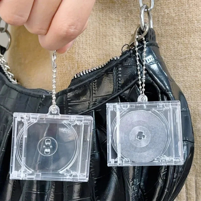 A clear plastic CD keychain is hanging from a silver chain attached to a black leather bag.