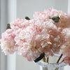 A close-up of a pink silk hydrangea stem with vintage burnt edge petals in a clear glass vase.