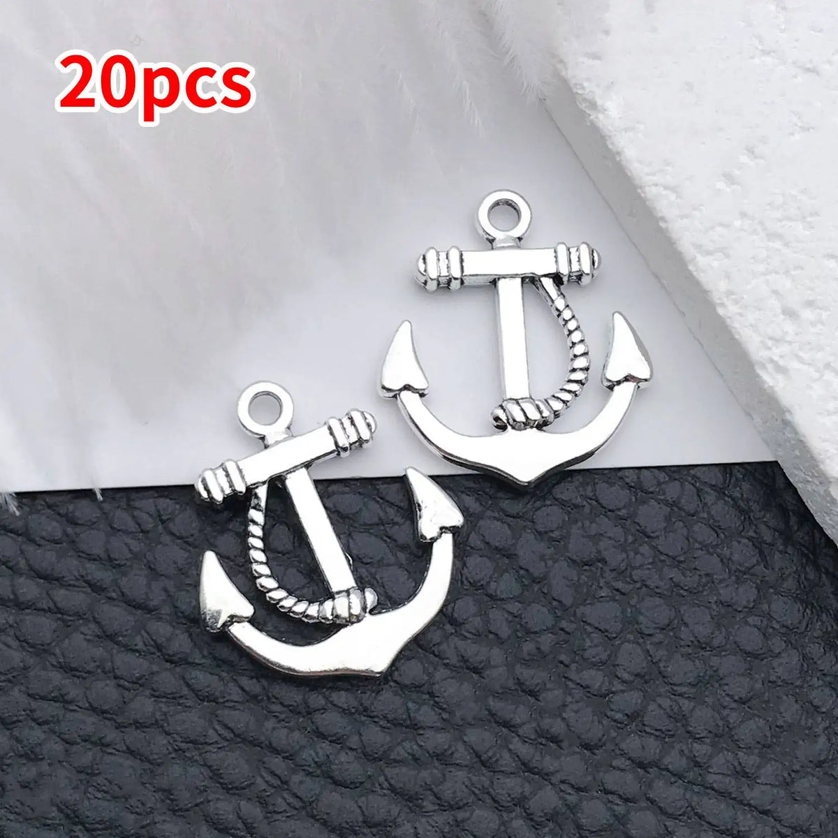 A pair of silver vintage ship anchor charms displayed on a black leather surface.