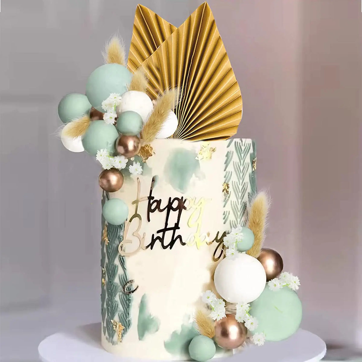 A tiered cake decorated with light green and gold accents, featuring palm leaf toppers and floral elements.
