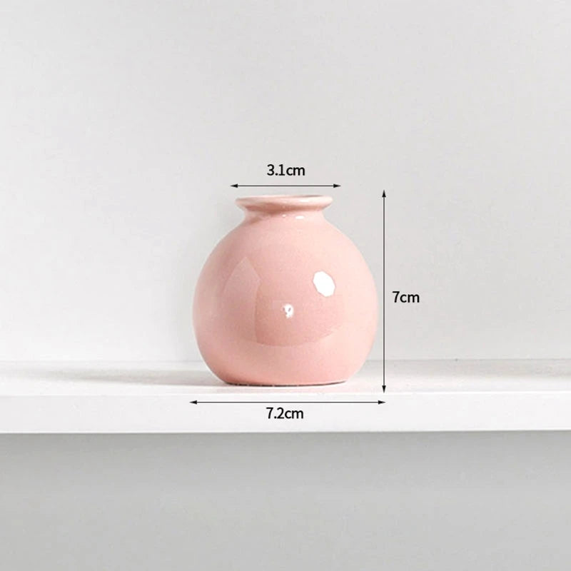 A pink ceramic mini vase with a rounded body and narrow neck, shown on a white shelf.