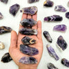 A hand holds several raw purple amethyst crystal stones on a white background.