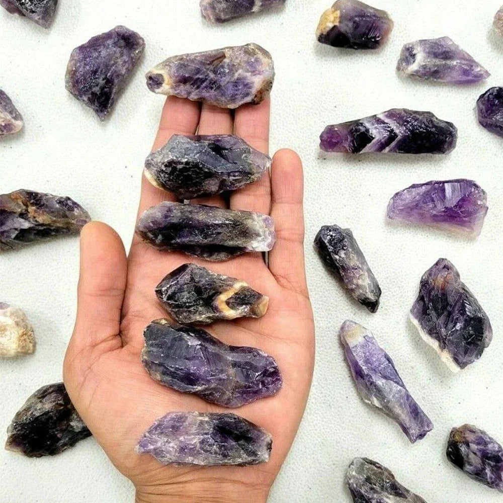 A hand holds several raw purple amethyst crystal stones on a white background.