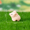 A small, light pink ceramic pig figurine placed on green grass.