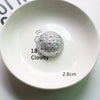 Une décoration sphérique argentée étiquetée 18 Clouday est placée sur une assiette en céramique blanche.