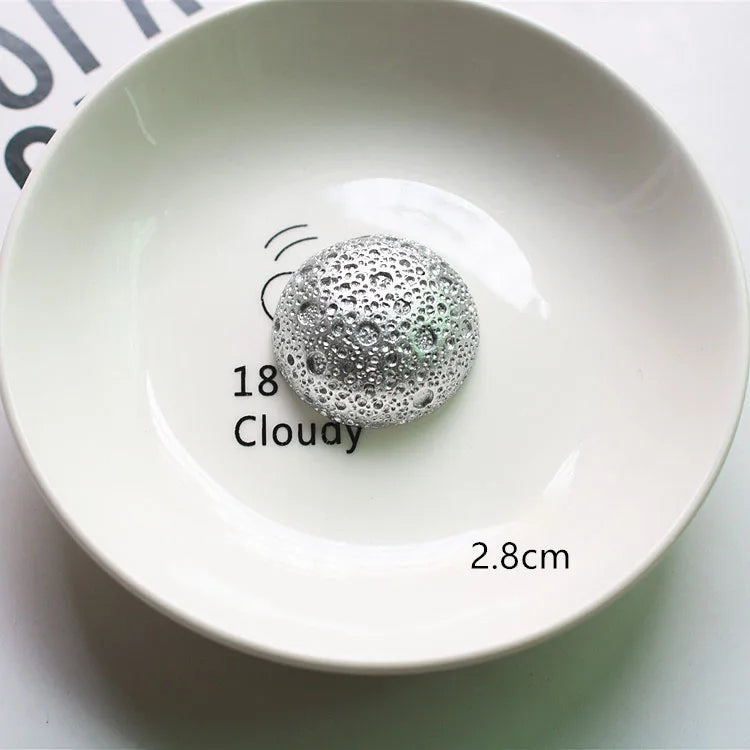 Une décoration sphérique argentée étiquetée 18 Clouday est placée sur une assiette en céramique blanche.