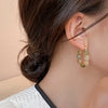 Gold and green resin beaded drop earrings worn by a woman