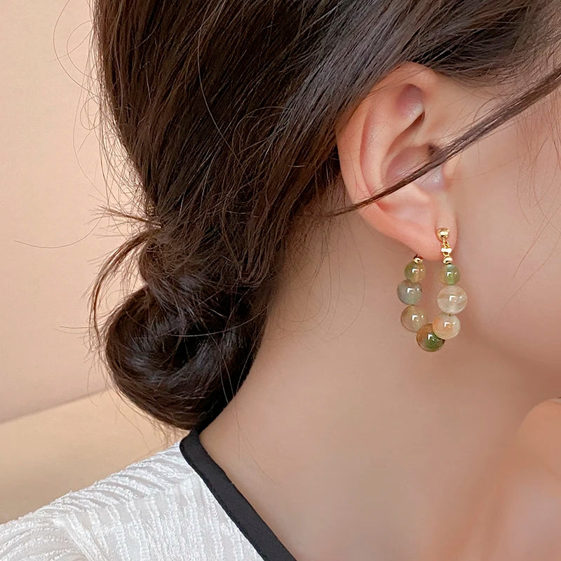 Gold and green resin beaded drop earrings worn by a woman