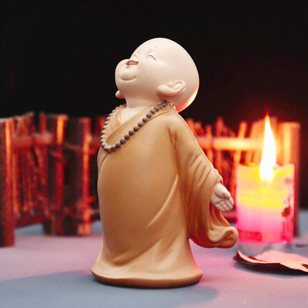 A small, smooth, tan resin figurine of a monk in robes is lit by a nearby candle.