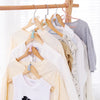 A collection of light-colored and gray t-shirts hanging on wooden hangers.