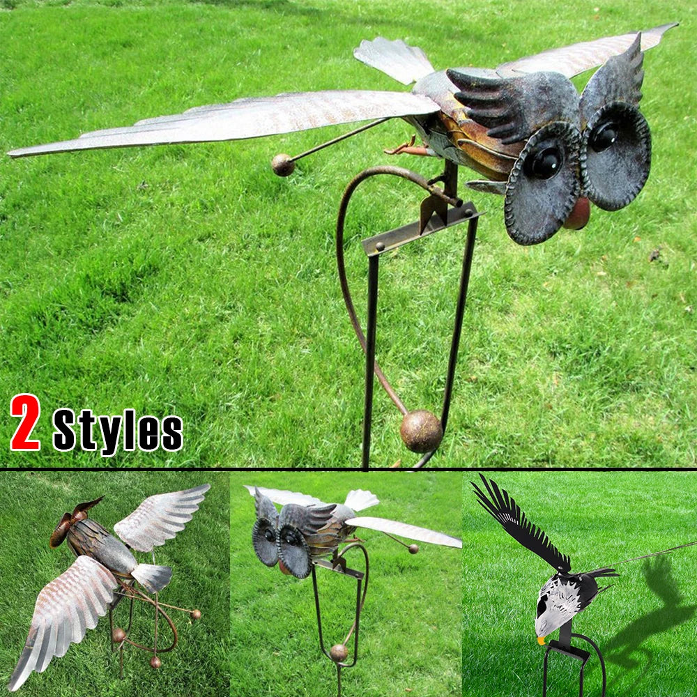 A wind spinner garden decoration featuring a bird sculpture with wings and a metal frame set in green grass.