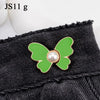 A close-up of a green butterfly with a pearl center attached to black denim fabric.