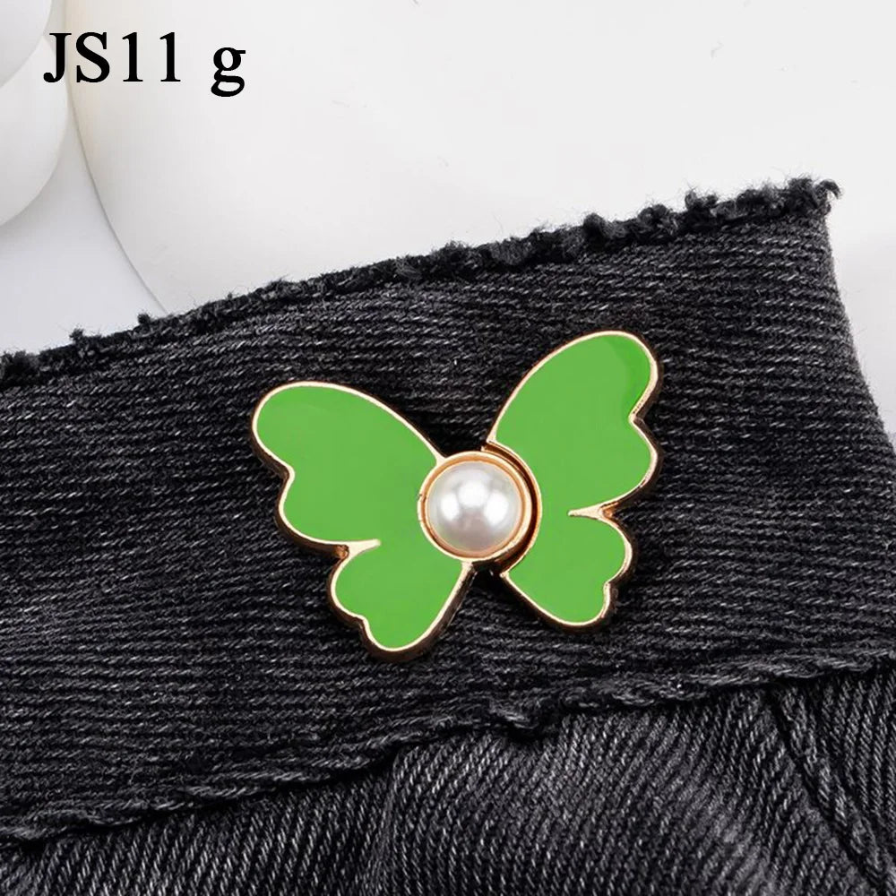 A close-up of a green butterfly with a pearl center attached to black denim fabric.