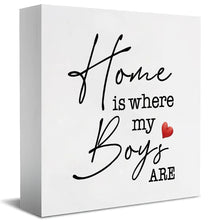 A white rectangular sign with black script that reads Home is where my Boys are and a red heart.
