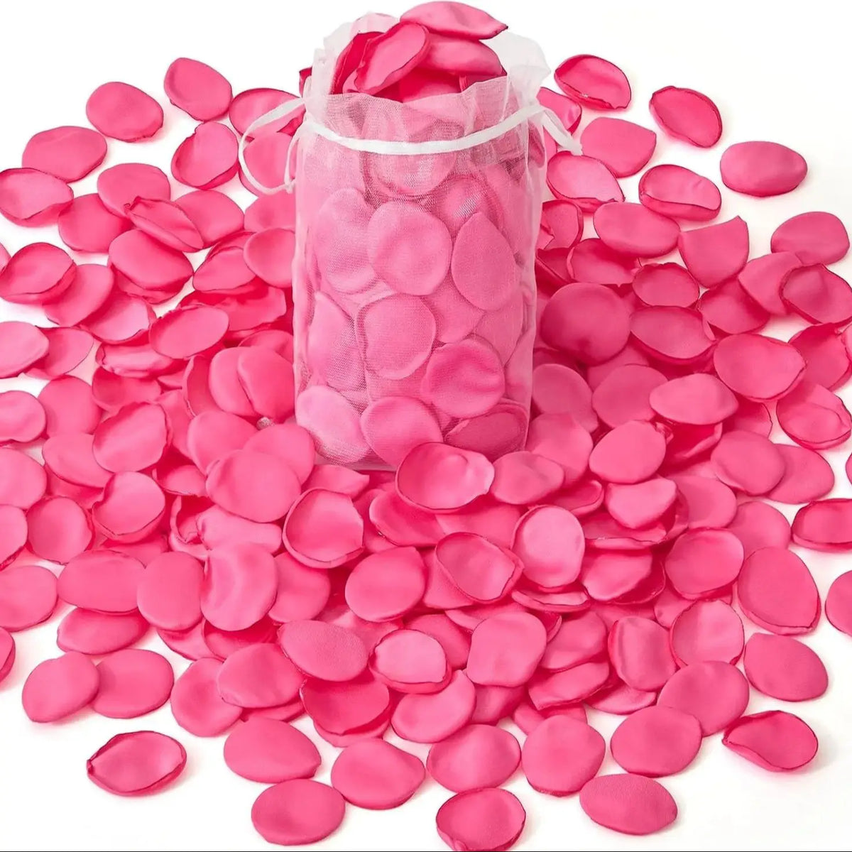 Una bolsa transparente llena de pétalos de flores artificiales rosas esparcidos sobre una superficie blanca.