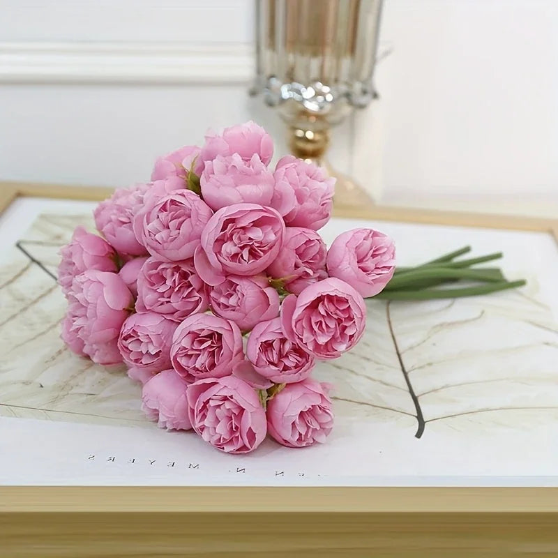 A bouquet of pink silk peonies with green stems displayed on a white surface.