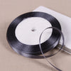 A black satin ribbon spool with a thin ribbon unwound on a light beige surface.