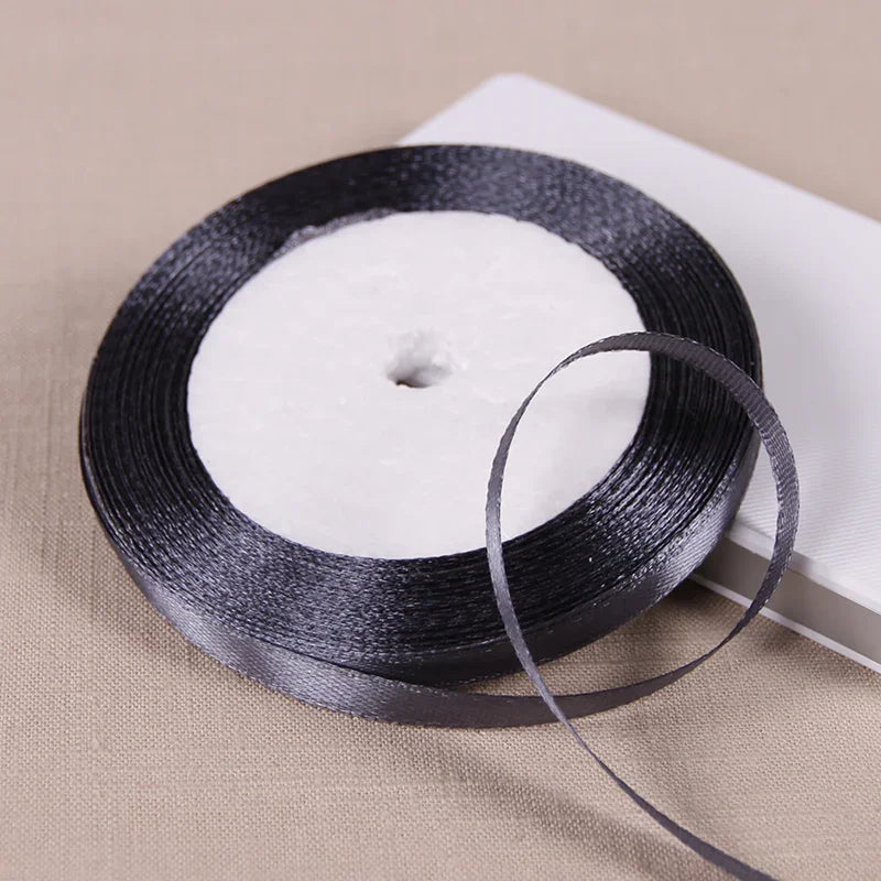 A black satin ribbon spool with a thin ribbon unwound on a light beige surface.
