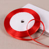 A spool of red satin ribbon with a white center, lying on a light surface.