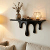A black drip floating shelf displaying decorative stones and a glass lantern on a white wall.