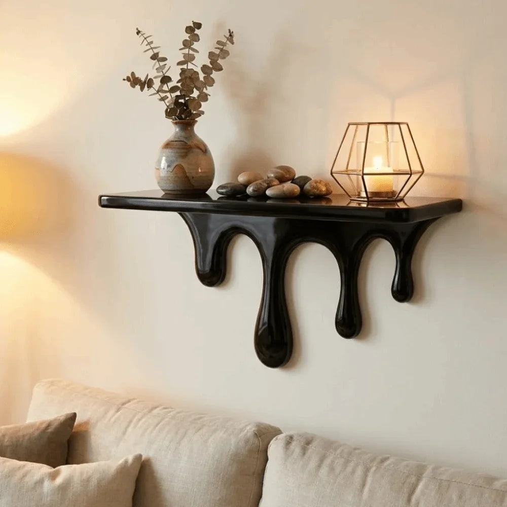 A black drip floating shelf displaying decorative stones and a glass lantern on a white wall.