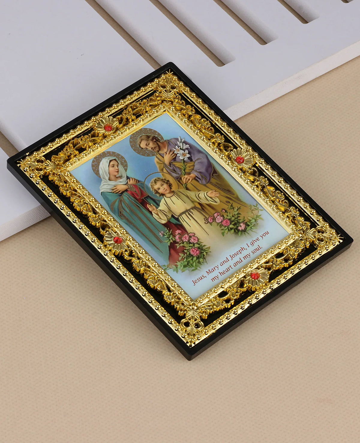 A framed icon depicting Jesus, Mary, and Joseph with an angel, set in a gold-edged black frame.