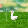A white duck figurine standing on green grass with measurement lines.
