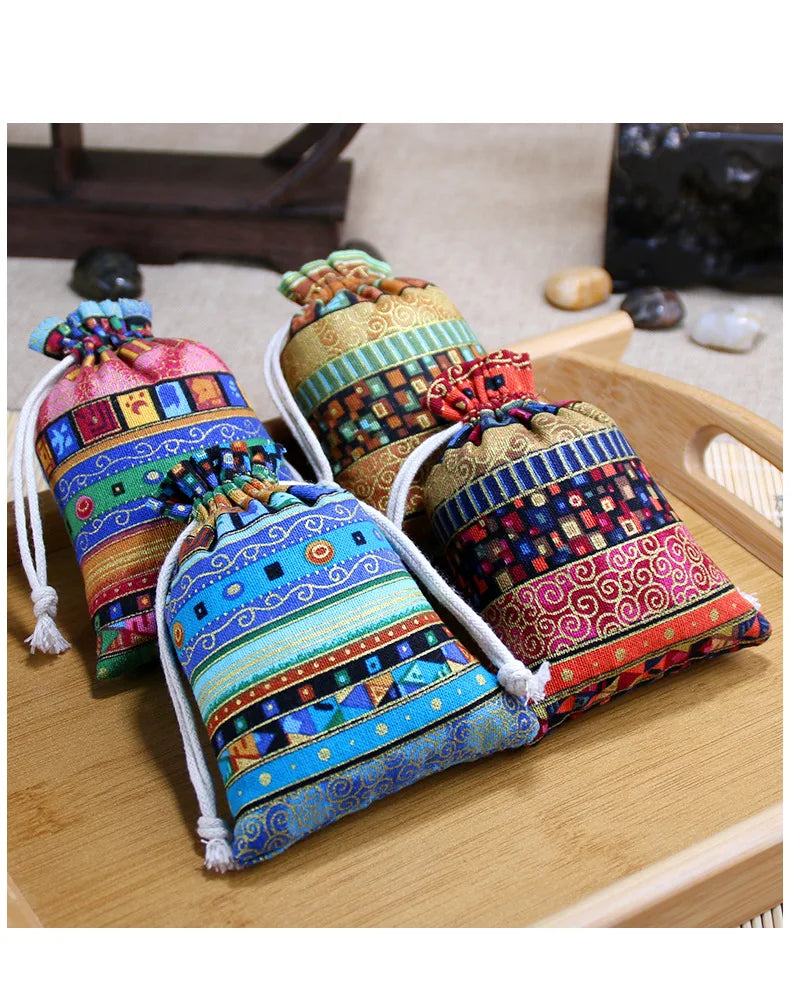 A set of ten vintage cotton drawstring gift pouches in various colorful patterns and textures resting on a wooden surface.