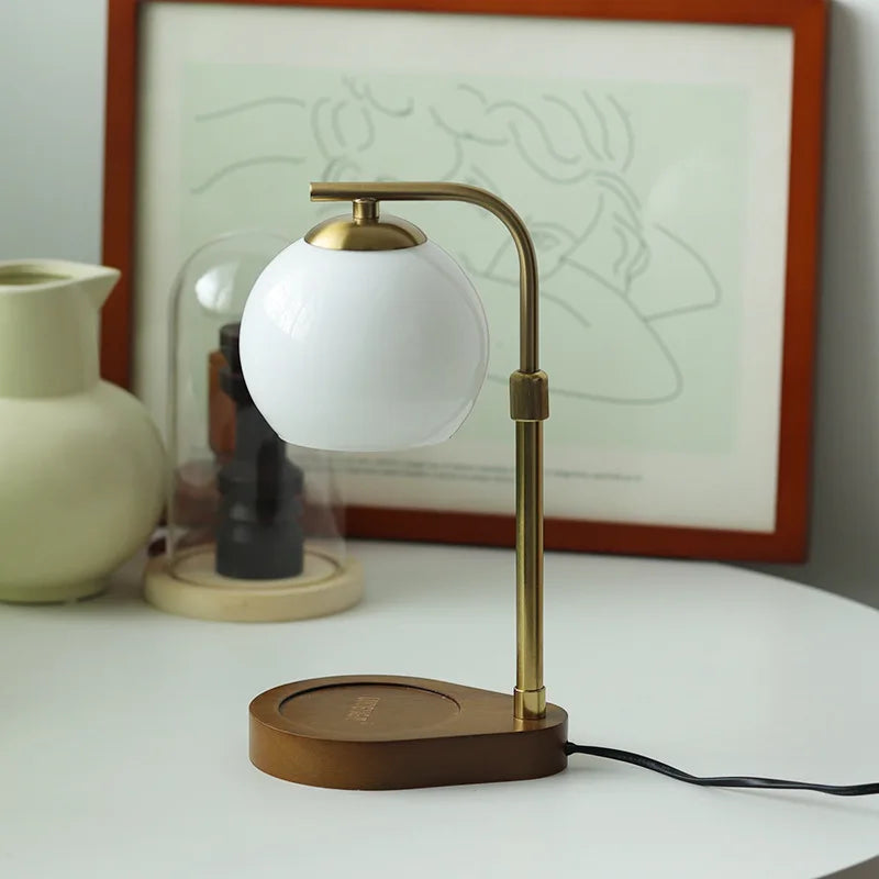 A brass aromatherapy wax melting lamp with a white spherical light is displayed on a white surface.
