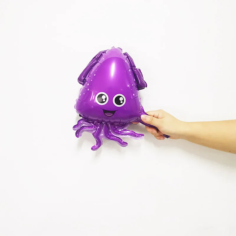 A purple foil balloon shaped like an octopus is being held by a hand against a white background.