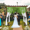 A wedding ceremony setup featuring an arbor decorated with artificial ivy garlands and white drapery.