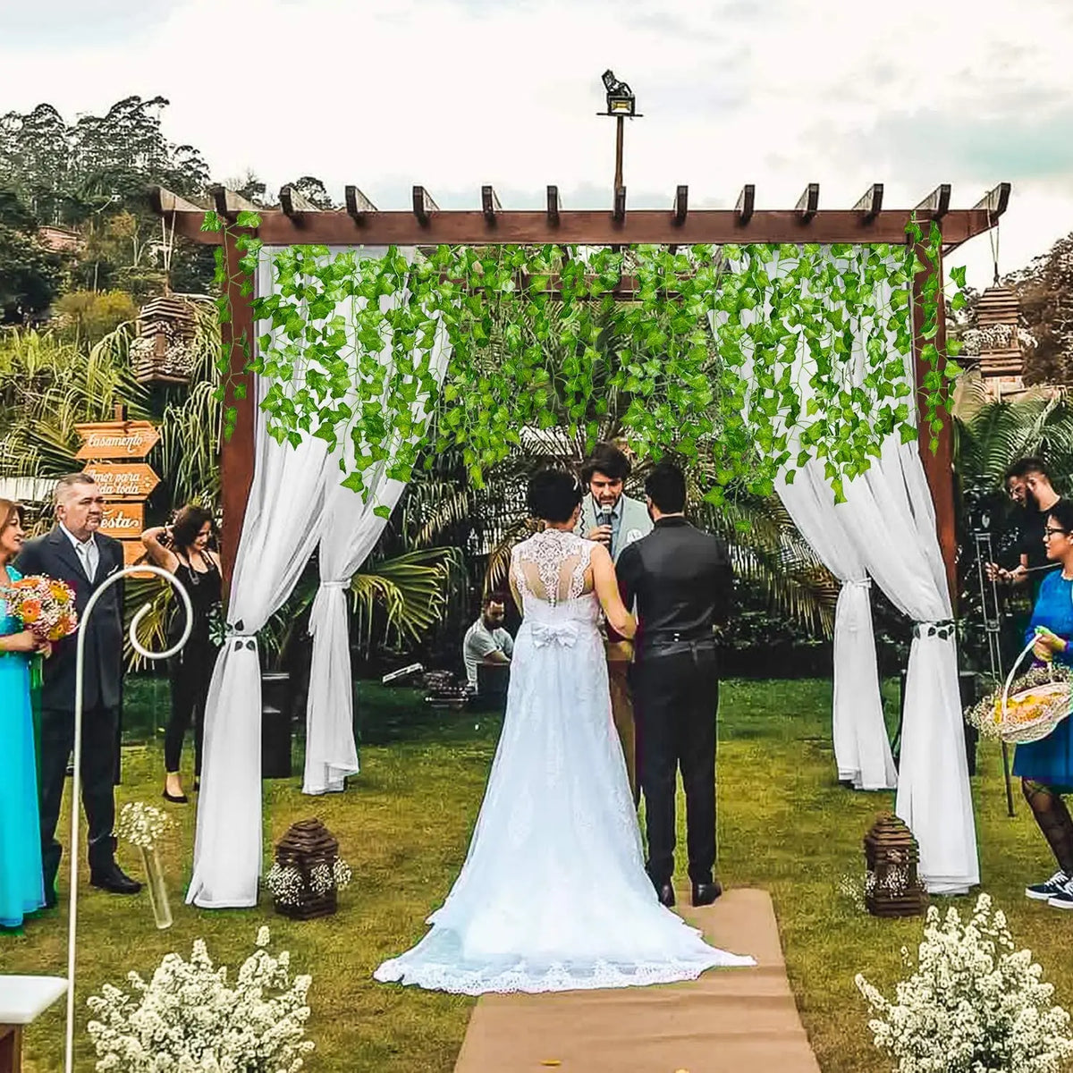 A wedding ceremony setup featuring an arbor decorated with artificial ivy garlands and white drapery.