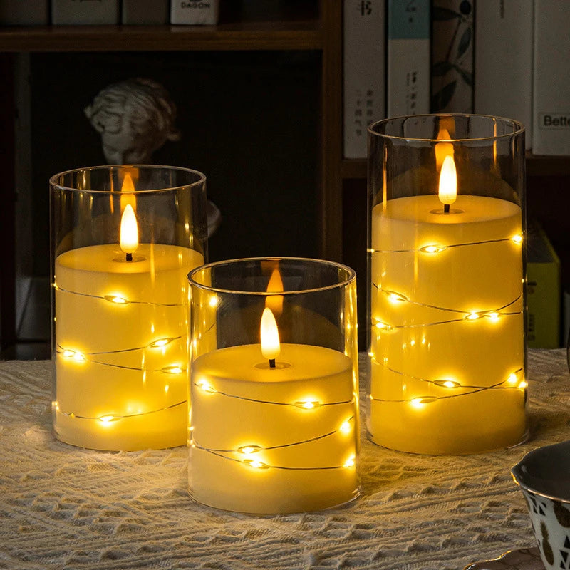 Three glass cylindrical candles with glowing LED star string lights on a woven fabric surface.
