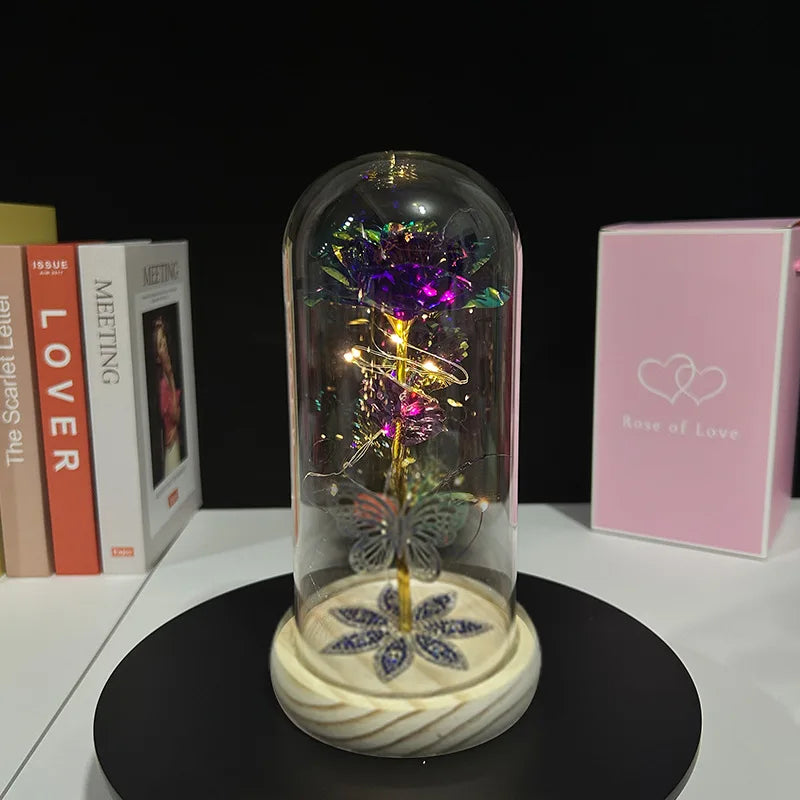 A rose crystal flower is displayed inside an illuminated glass dome on a black stand.