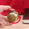 A hand holds a round, golden Chinese lucky coin spinner fidget toy against a red background.