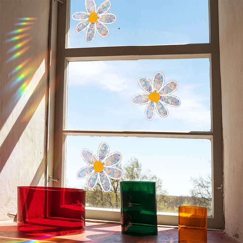 A window features three daisy flower sun catchers, including blue and white glass flowers, casting rainbows onto the interior