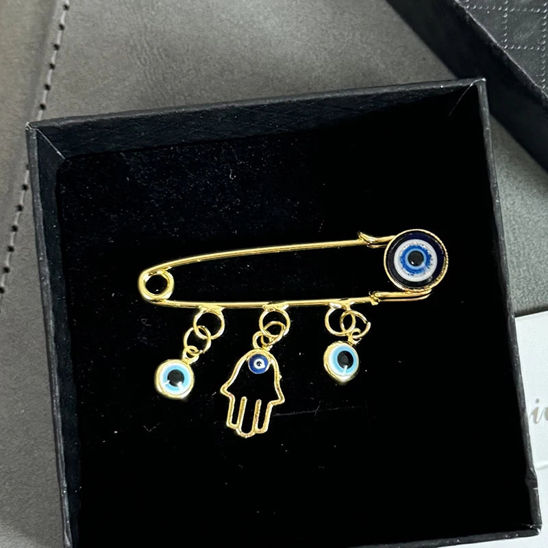 Elegant gold and silver evil eye brooch pin featuring a hand shape and an eye design.