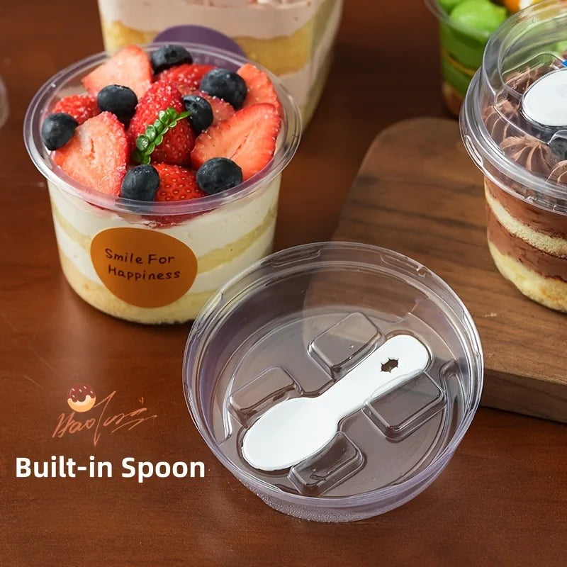 A clear reusable pudding cup with a built-in spoon is shown next to a serving of strawberry and blueberry dessert.