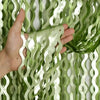 Sage green wavy foil fringe curtain streamers being held by a hand
