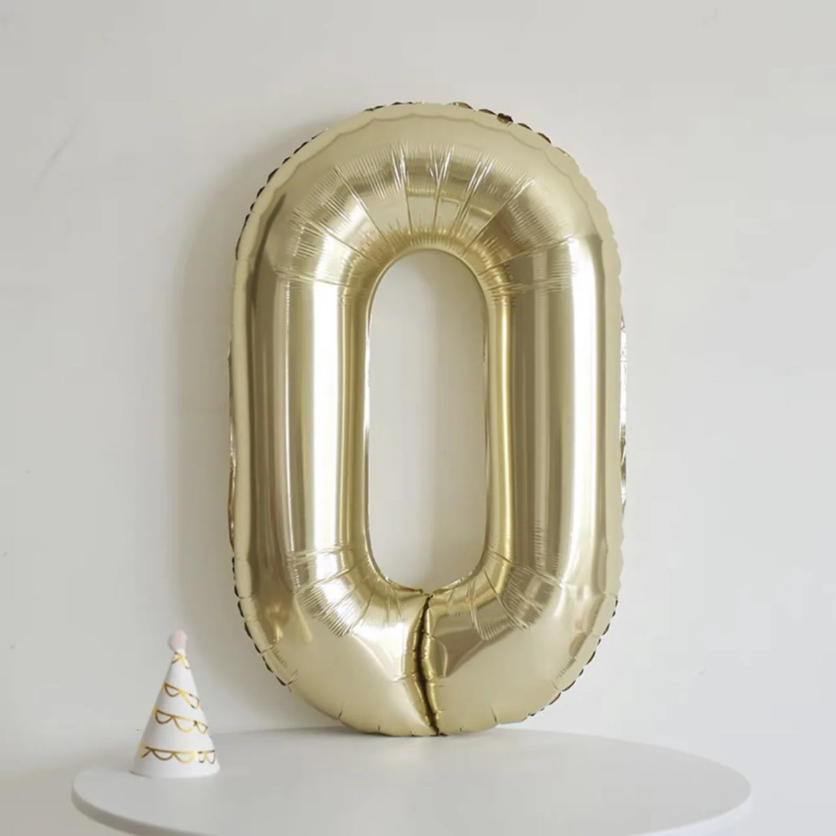 A large gold foil number balloon shaped like the digit zero displayed against a white background.
