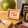 A wooden photo frame displaying a small colorful photograph on a light wood surface.
