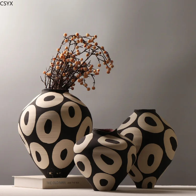 A black and white ceramic vase with a geometric circle design sits on a white surface.