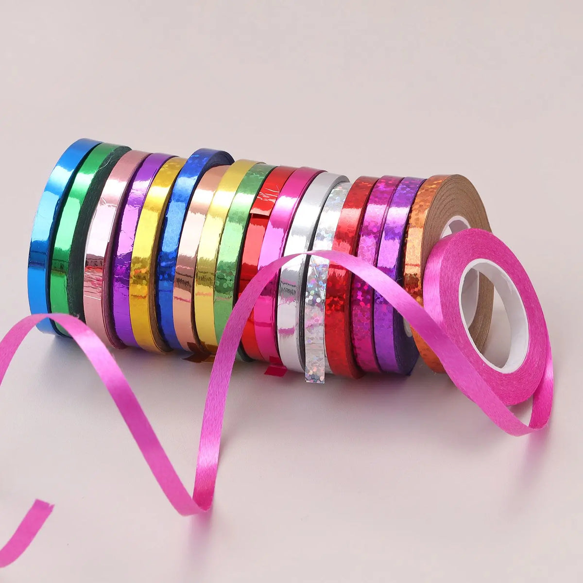 A collection of colorful satin balloon ribbon rolls in various shades are displayed on a white surface.