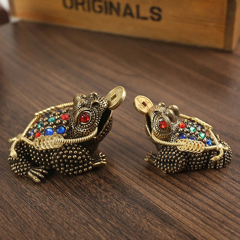 Un par de sapos de la suerte chinos de color dorado adornados con joyas de colores sobre una superficie de madera oscura.