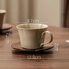 A beige ceramic coffee cup and saucer set displayed on a wooden surface.