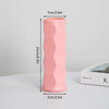 Eine hohe, rosa, zylindrische Plastikblumenvase mit glatter Textur neben einer Box.