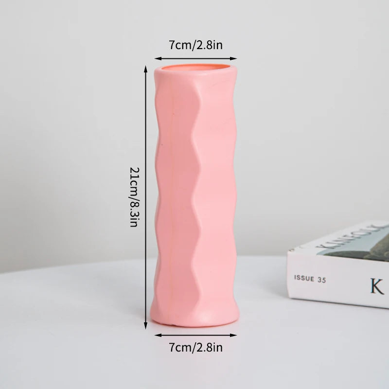 Eine hohe, rosa, zylindrische Plastikblumenvase mit glatter Textur neben einer Box.